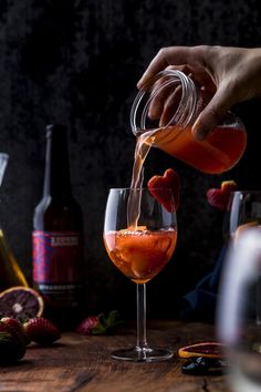 someone is pouring wine into a glass with strawberries on the table next to it