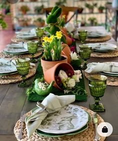 the table is set with green and white plates, silverware, and flowers in pots