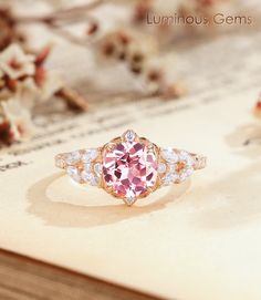 a pink diamond ring sitting on top of a piece of paper with flowers in the background