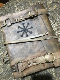 an old leather book sitting on top of a metal tray with straps and buckles