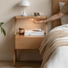 a person reaching for a book on a nightstand next to a bed