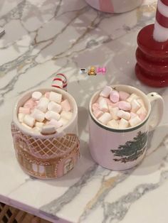 two mugs filled with marshmallows sitting on a table