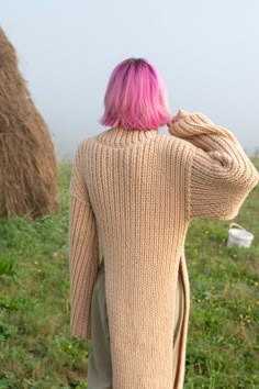 a woman with pink hair is standing in the grass and looking at hay bales