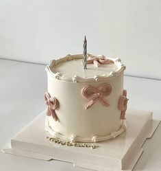 a white cake with pink bows and a single candle sitting on top of a book