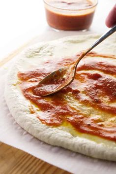 a person spooning sauce onto a pizza dough