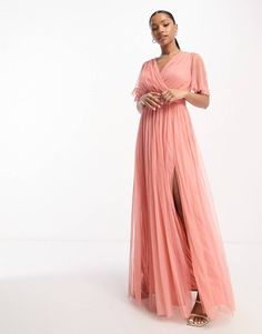 a woman in a long pink dress standing with her hands on her hips and looking off to the side