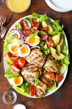 a white plate topped with meat, lettuce and tomato salad next to a fork