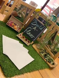 an arrangement of flowers and plants on display in front of a chalkboard sign that says build a plant