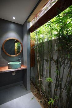 an outdoor bathroom with bamboo plants and a round mirror on the wall above the sink