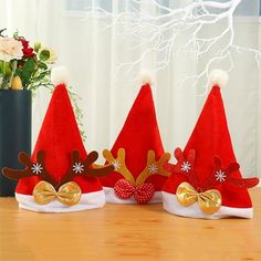 three red santa hats with gold bows and reindeer antlers on them sitting on a table