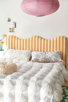 a bed with white and yellow striped headboard next to a pink light fixture above it