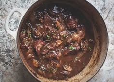 a pot filled with meat and mushrooms on top of a table