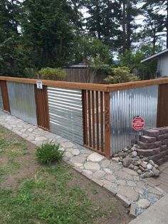 a fence made out of metal and wood in front of a yard with rocks on the ground