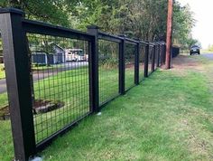 a black fence that is next to a road in the grass with cars parked on it