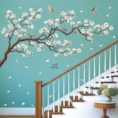 a tree with white flowers and birds painted on the wall next to a stair case