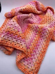 an orange and pink crocheted blanket laying on top of a table