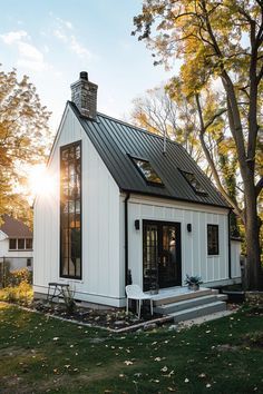 a small white house with a black roof in the fall sun shining on it's windows