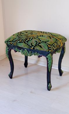 a green and black bench sitting on top of a hard wood floor next to a white wall