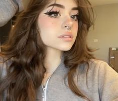 a woman with long brown hair and piercings on her nose wearing a grey sweatshirt