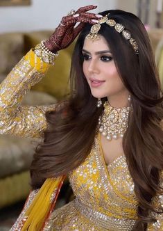 a woman in a yellow dress with long hair and jewelry on her head, posing for the camera