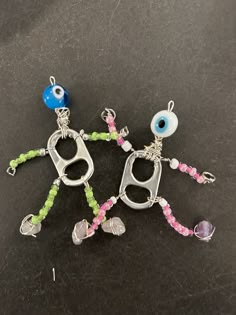 three charms with eyes and beads hanging from them on a black surface, one in the shape of a keychain