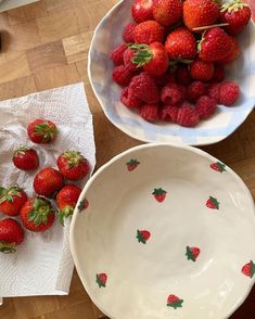 two white bowls filled with strawberries on top of a wooden table