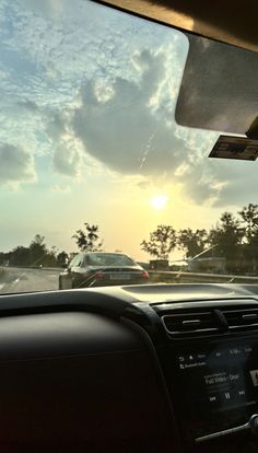 the sun is setting behind some cars driving down the road in traffic on a cloudy day