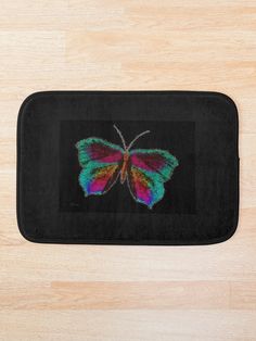 a bath mat with a colorful butterfly on the front and back side, sitting on top of a wooden floor