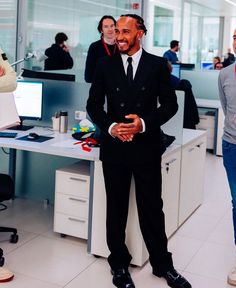 a man in a suit and tie standing next to a desk with people working on computers