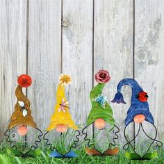 four little garden gnomes sitting in the grass with flowers on their heads and tails