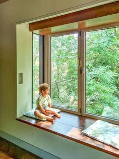 a young child sitting on a window sill looking out at the trees outside it