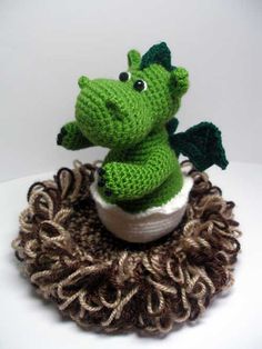 a crocheted green dragon sitting on top of a pile of brown and white yarn