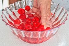 a person picking raspberries out of a bowl with their hands on the table