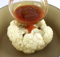 a bowl filled with cauliflower and sauce being poured on top of the cauliflower