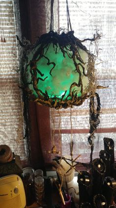 a green light hanging from the ceiling in front of a window with other items on it