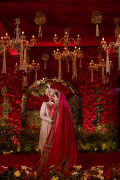 a bride and groom standing in front of a red wall with chandelier hanging from it