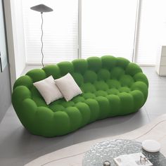 a green couch sitting on top of a living room floor next to a table with two white pillows