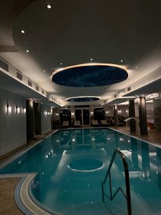 an indoor swimming pool in a hotel with blue water and lights on the ceiling above it