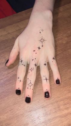 a person's hand with black nail polish and cross tattoos on it, sitting at a wooden table