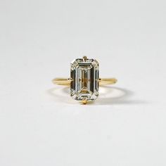 an emerald cut diamond ring on a white surface with the center stone in yellow gold