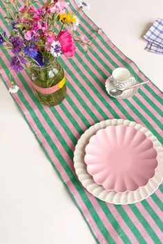 a pink plate sitting on top of a green and white striped table cloth next to a vase filled with flowers