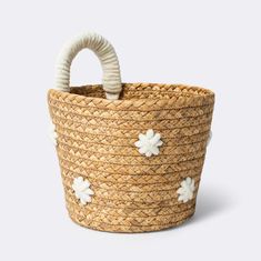 a woven basket with white flowers on the handle and handles, sitting in front of a gray background