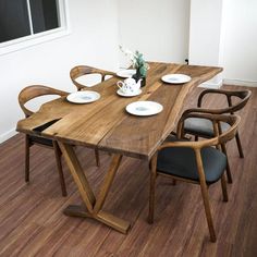 a wooden table with four chairs around it and plates on the table in front of it