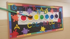 a colorful bulletin board with paint and brushes on it in a school hallway or classroom room