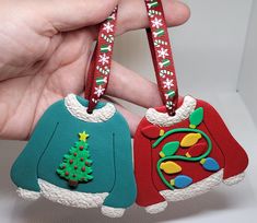 two handmade christmas sweater ornament hanging from a red and green ribbon in front of a white background