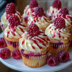 cupcakes with raspberries and cream frosting on a white cake plate