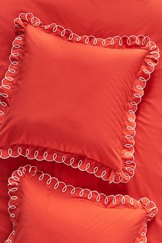 three red pillows with white piping on top of each pillow and the bottom one has an orange comforter