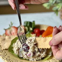 a person is holding a fork over a plate of food with fruit and crackers