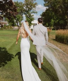 the bride and groom are walking through the grass with their veil blowing in the wind