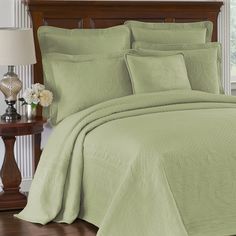 a bed with green bedspread and pillows in a room next to a night stand